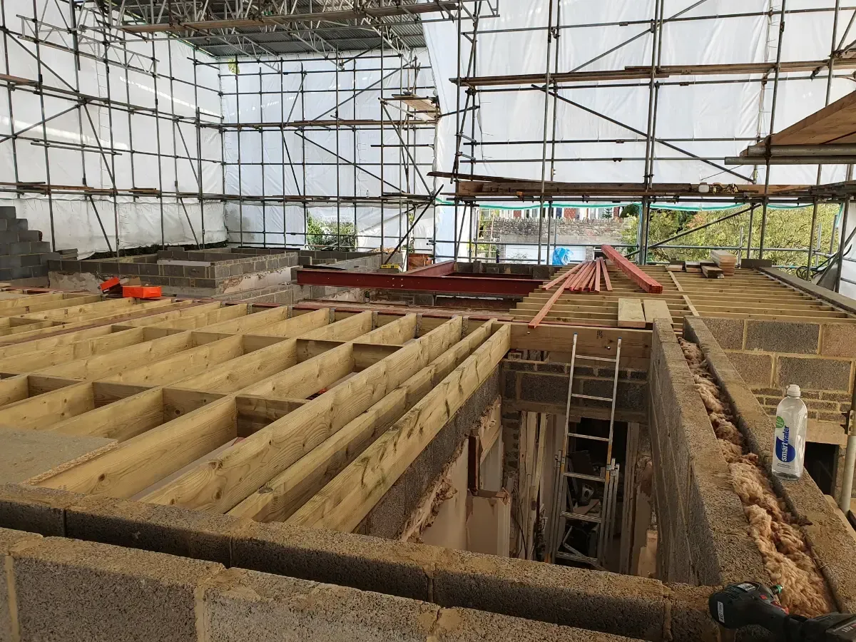 Construction site with rebar framework, wooden forms, and a partially excavated floor under scaffolding