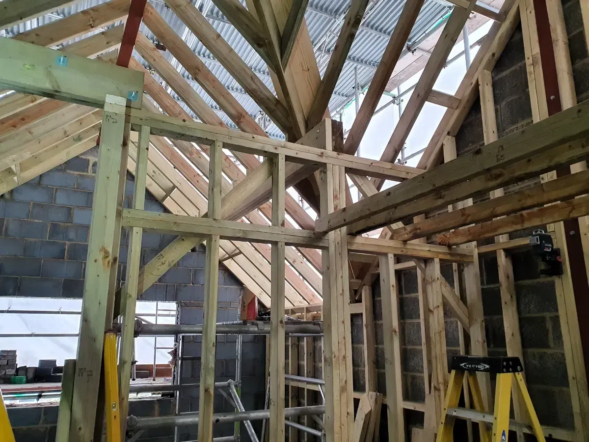 Unfinished house interior with exposed wooden roof trusses and wall framing under construction.
