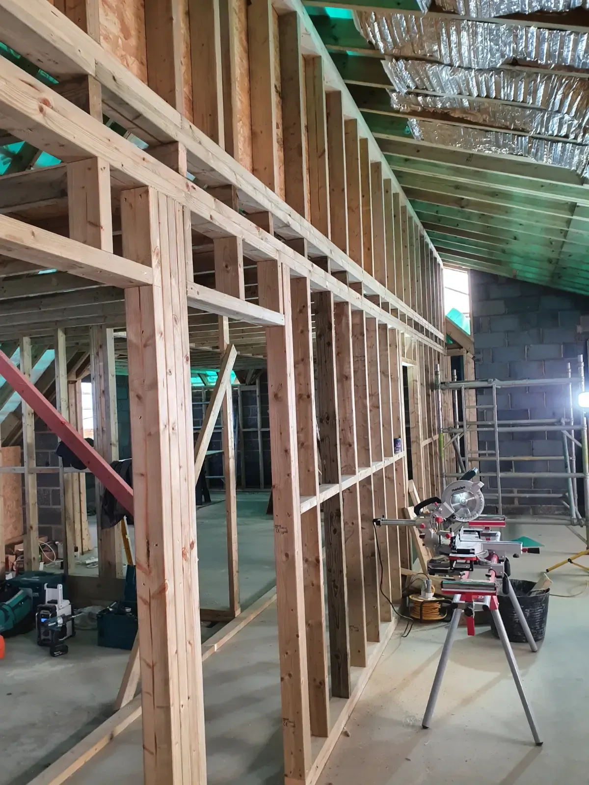Wood-framed interior construction site with exposed studs, tools, and a bright work light in the back.