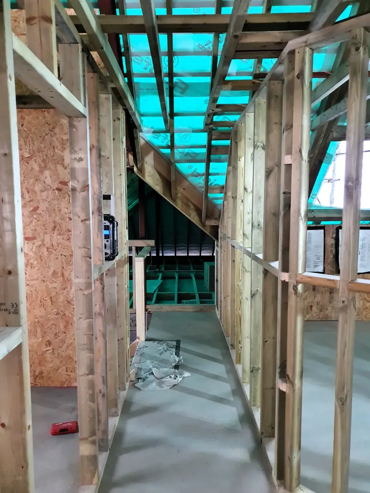 Interior of a framed hallway under construction, with exposed wood studs and a blue-tarp roof.