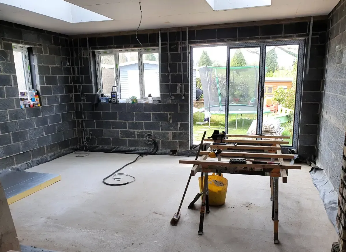 Partially renovated room with black block walls, large windows, and a workbench in the foreground