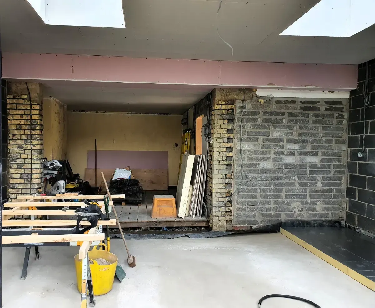 Indoor renovation site with exposed brick walls, construction materials, and unfinished ceiling.