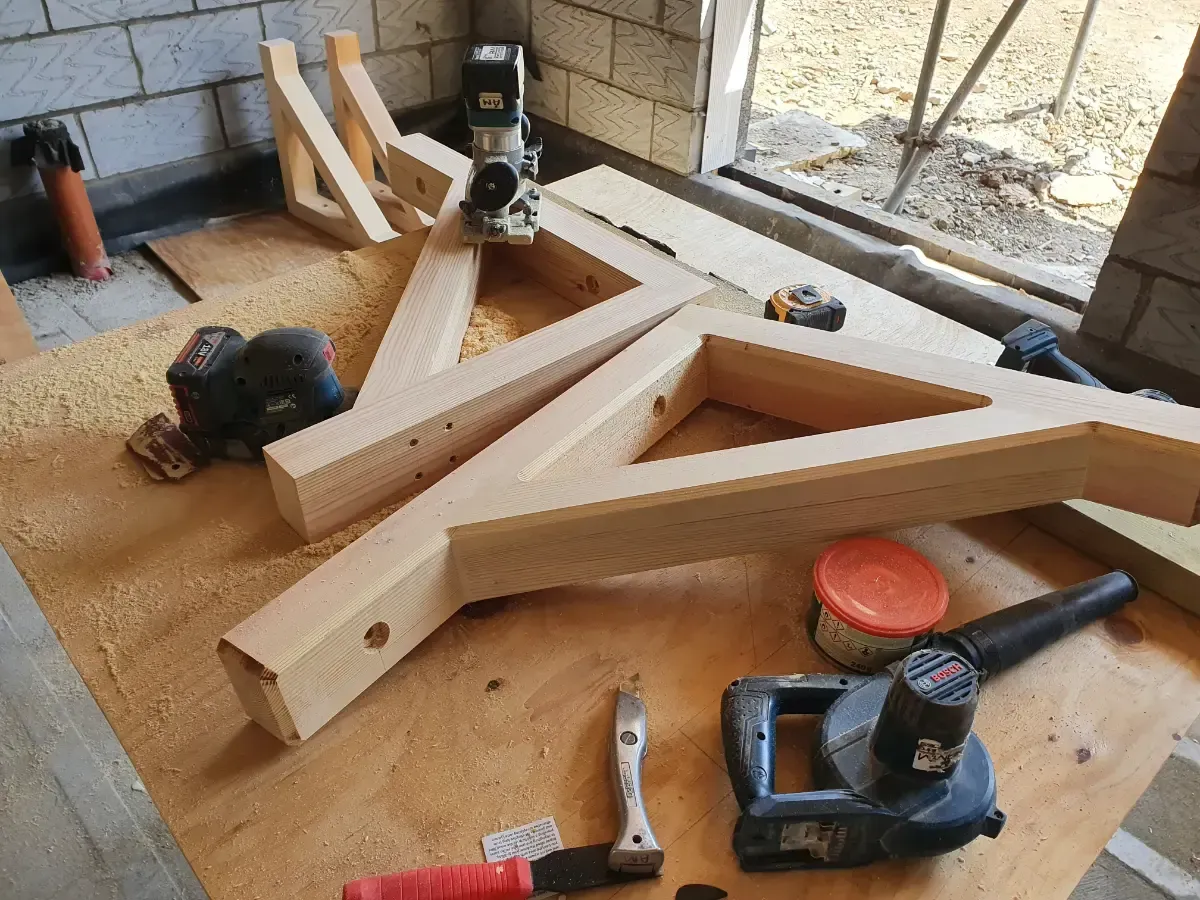 Wooden triangular frame pieces on a workbench with a drill, hammer, and saw in a workshop area