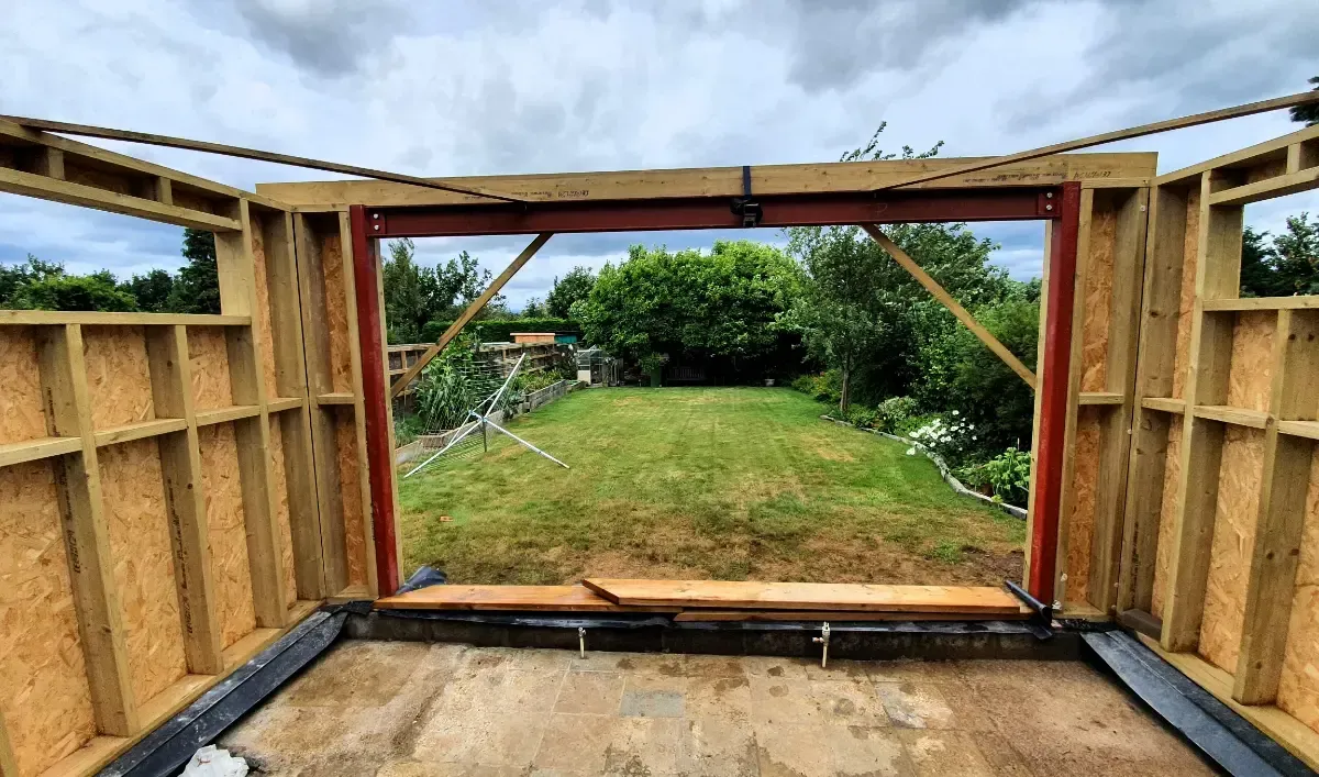 Partially built wooden structure framing a grassy backyard under a cloudy sky