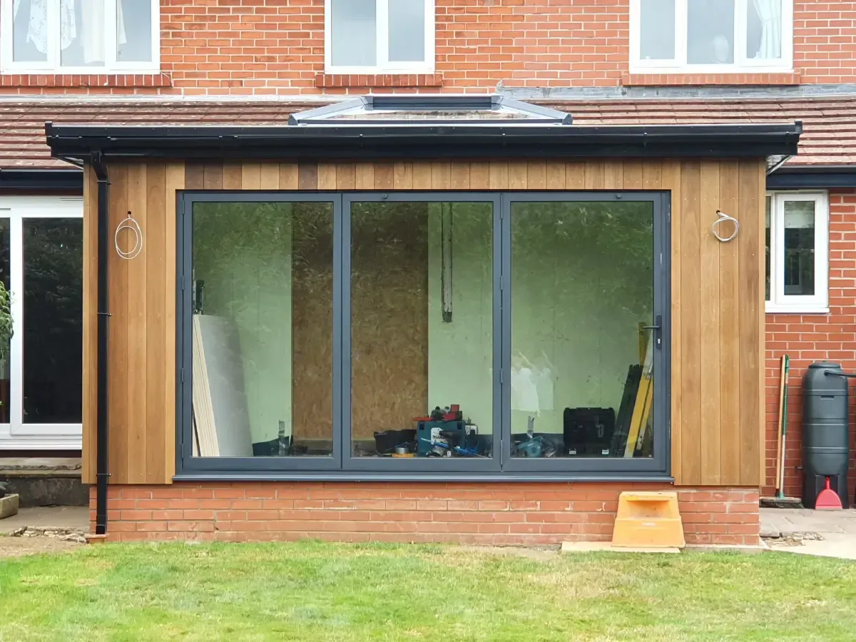 Modern backyard sunroom with large windows and wood siding attached to a brick house
