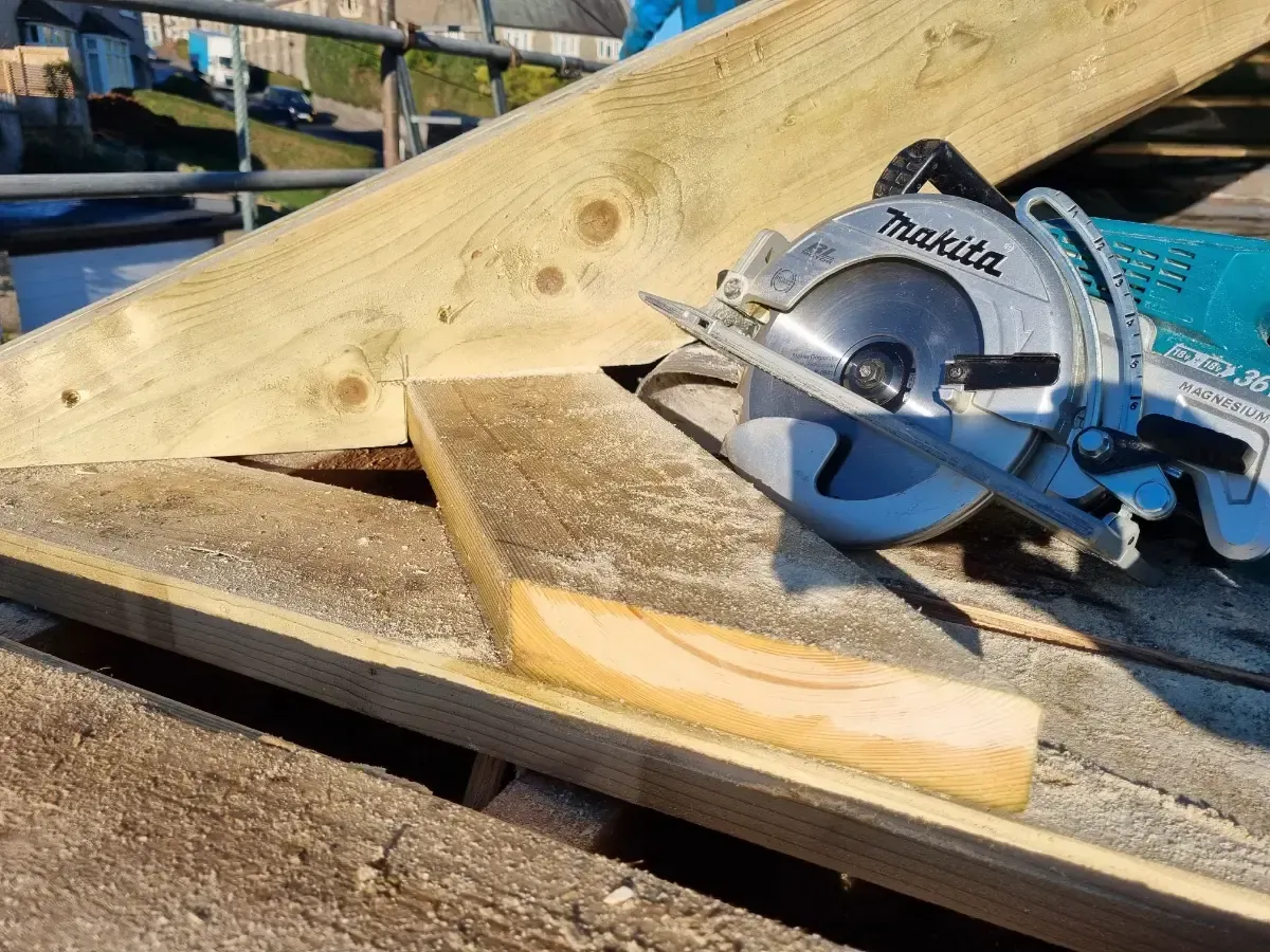 Circular saw on a wooden plank at a construction site, cutting lumber on a slanted frame.