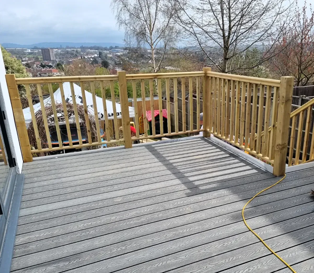Wooden deck with railing overlooking a distant hillside town on a clear day.