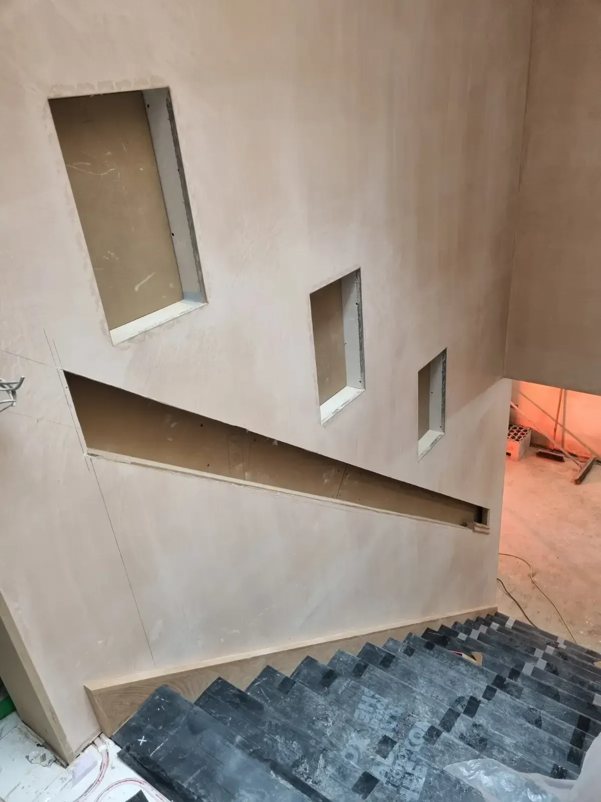Indoor stairwell with dark steps, beige walls, rectangular windows, and a slanted handrail cutout.