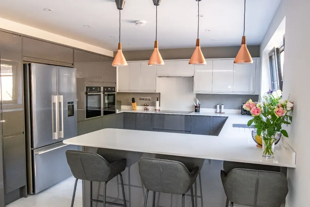 Modern kitchen with white island, gray stools, stainless steel appliances, and copper pendant lights