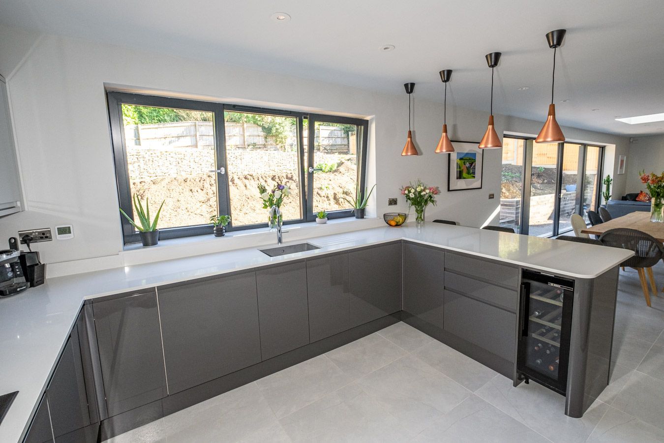 Modern L-shaped kitchen with gray cabinets, white countertops, pendant lights, and large window over the sink