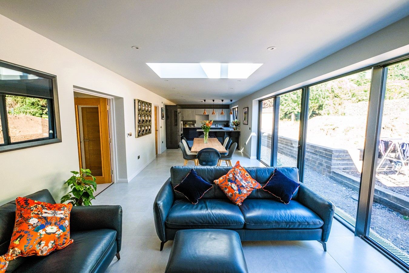 Bright modern living room with black leather sofa, skylights, and sliding glass doors overlooking greenery