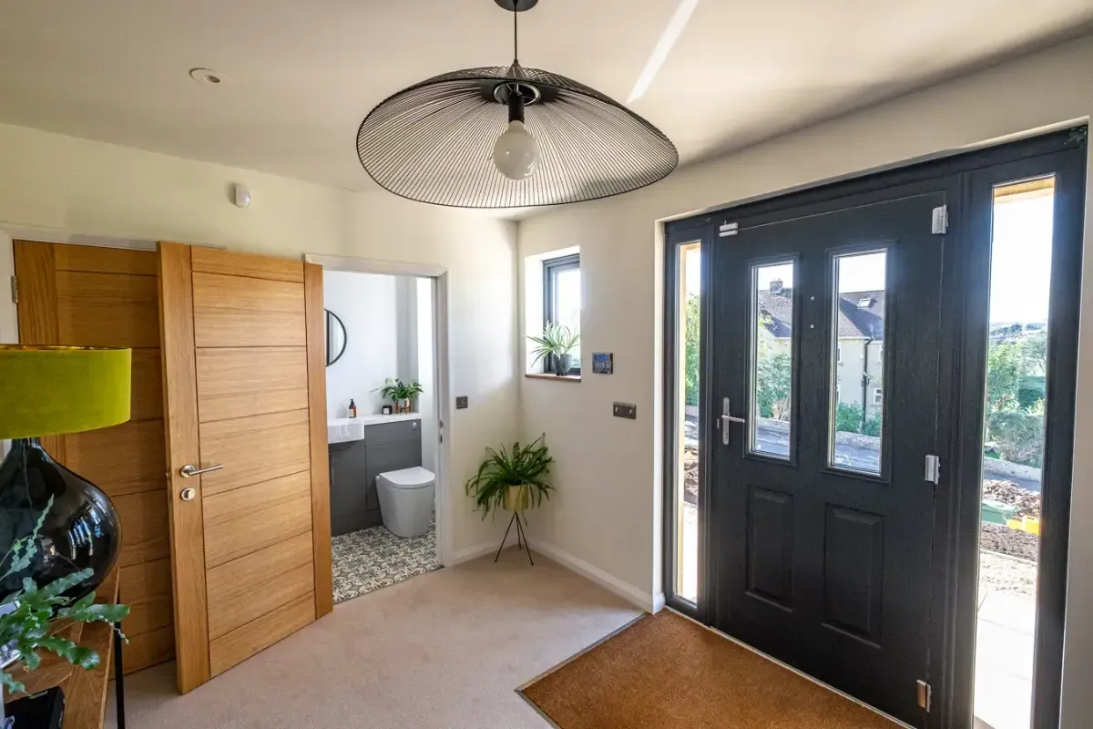 Bright entryway with black front door, wooden closet, and ceiling light, opening to a small bathroom.