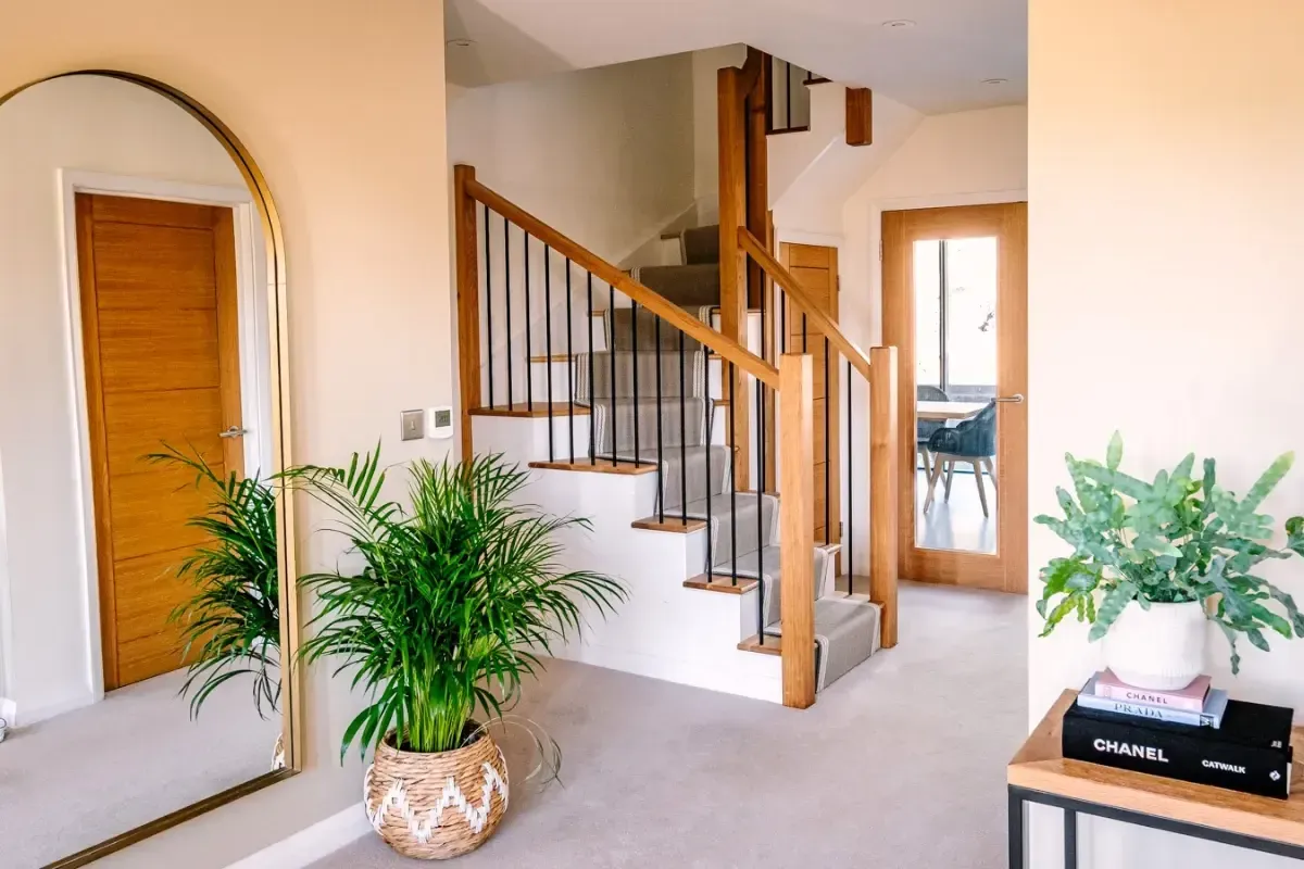 Bright foyer with staircase, arched mirror, potted plants, and wooden door