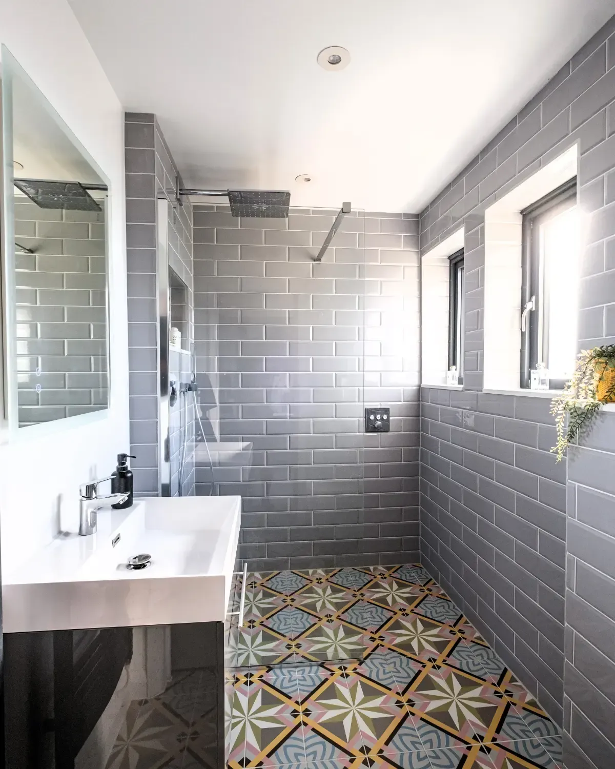 Modern bathroom with gray subway tiles, patterned floor, white vanity, mirror, and shower area