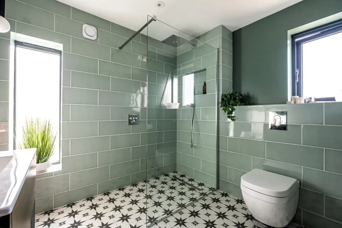 Bright green-tiled bathroom with a walk-in shower, toilet, and small windows.