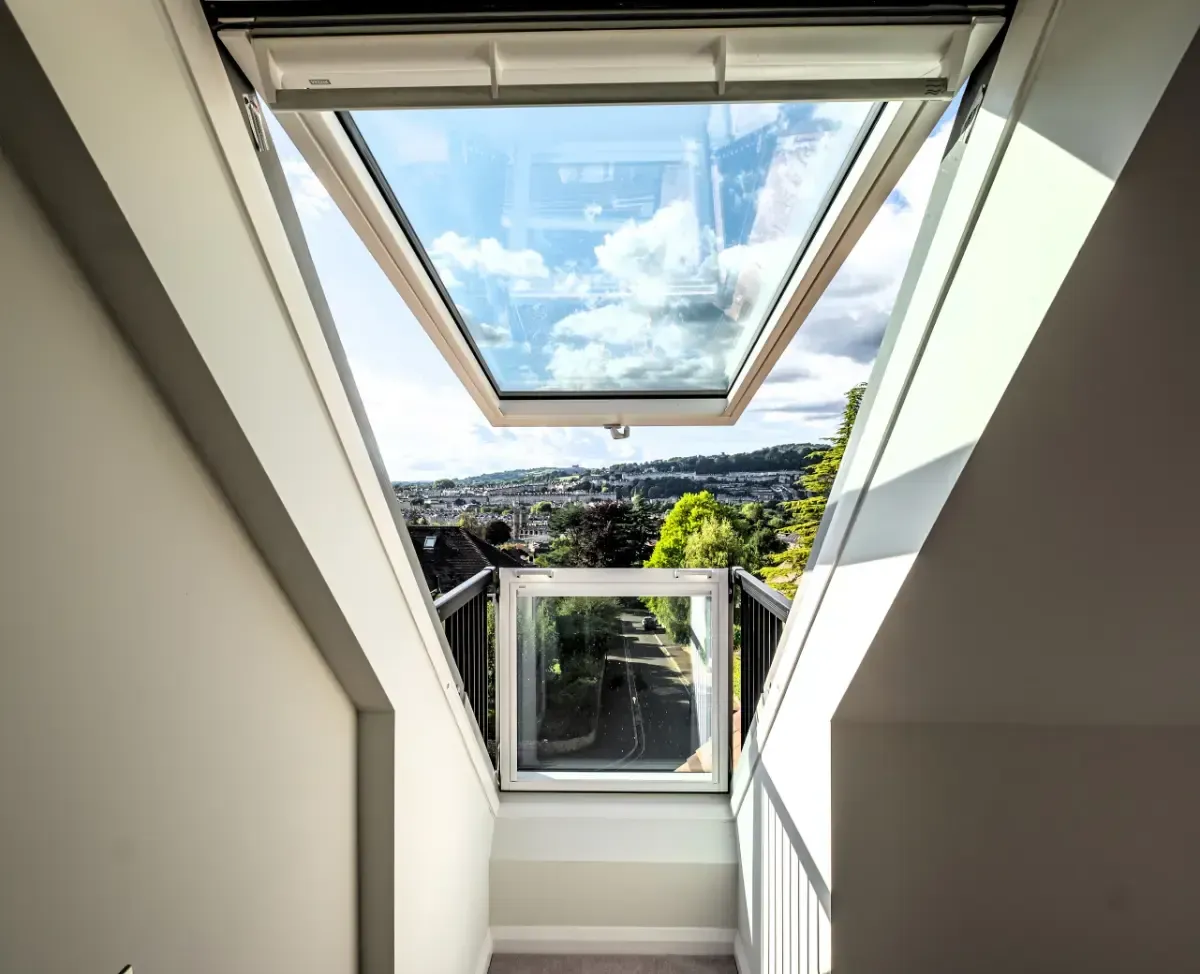 Skylight stairwell with open windows and a view of blue sky, clouds, and a distant city