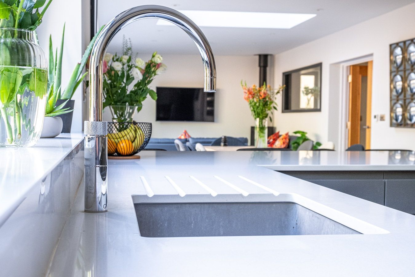 Modern kitchen with white countertops, chrome faucet, and flowers by a window