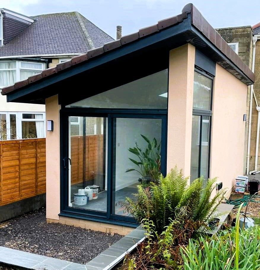 Modern garden room with black-framed glass doors and slanted roof in a residential backyard