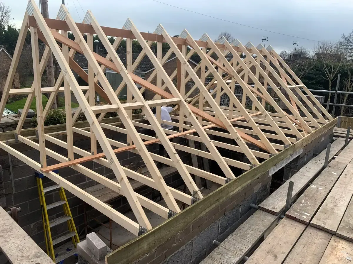 Roof trusses under construction on a building, with wooden beams and a cloudy sky.