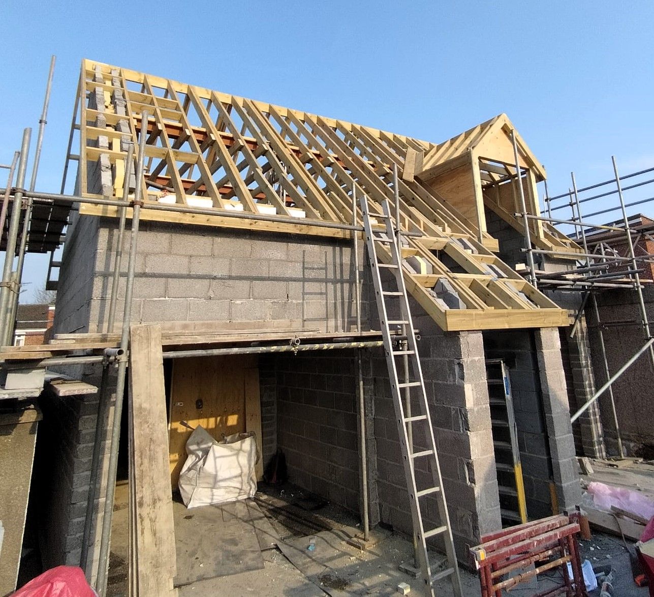 Partially built house with wooden roof framing, concrete walls, and scaffolding under construction