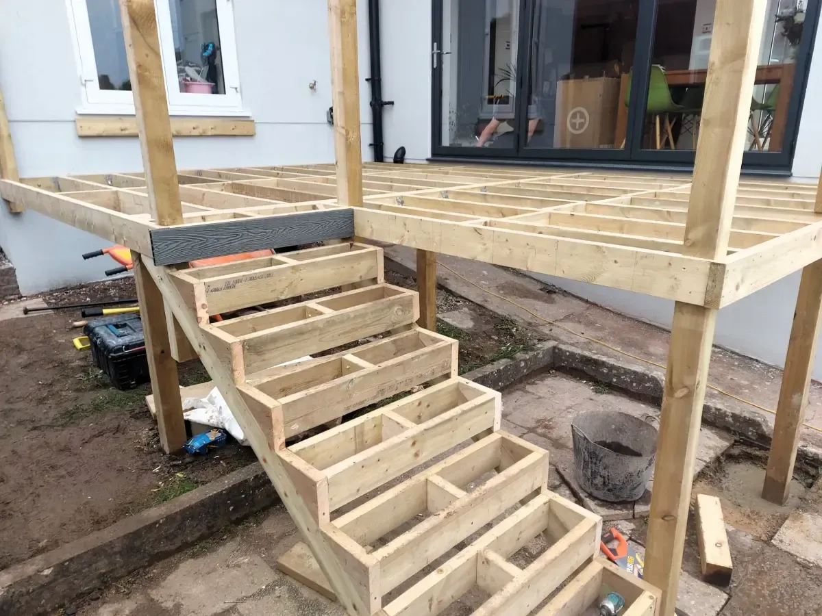 Wooden porch stairs under construction beside a house, with unfinished railings and deck posts.