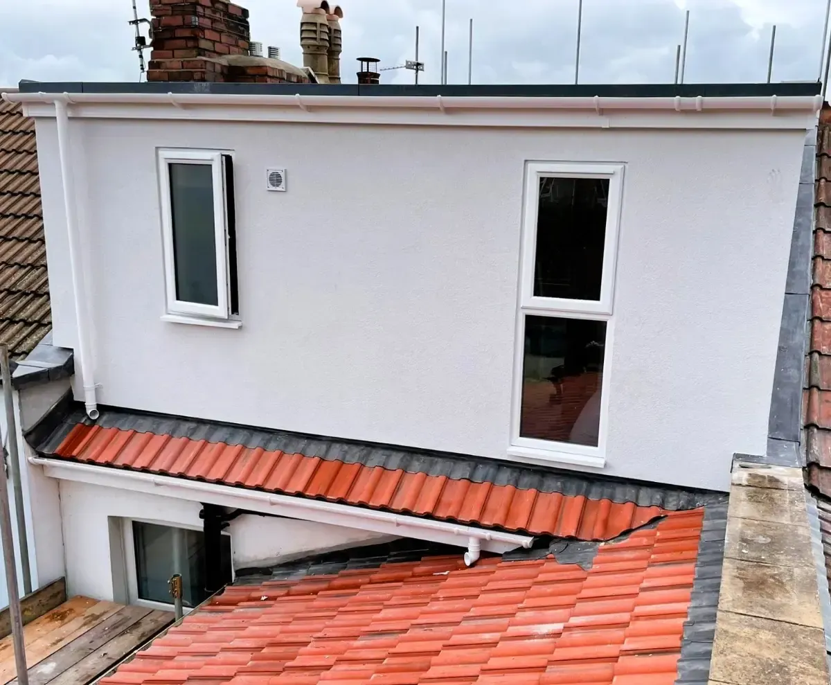 White building wall with two windows above red-tiled roofs and a slanted awning