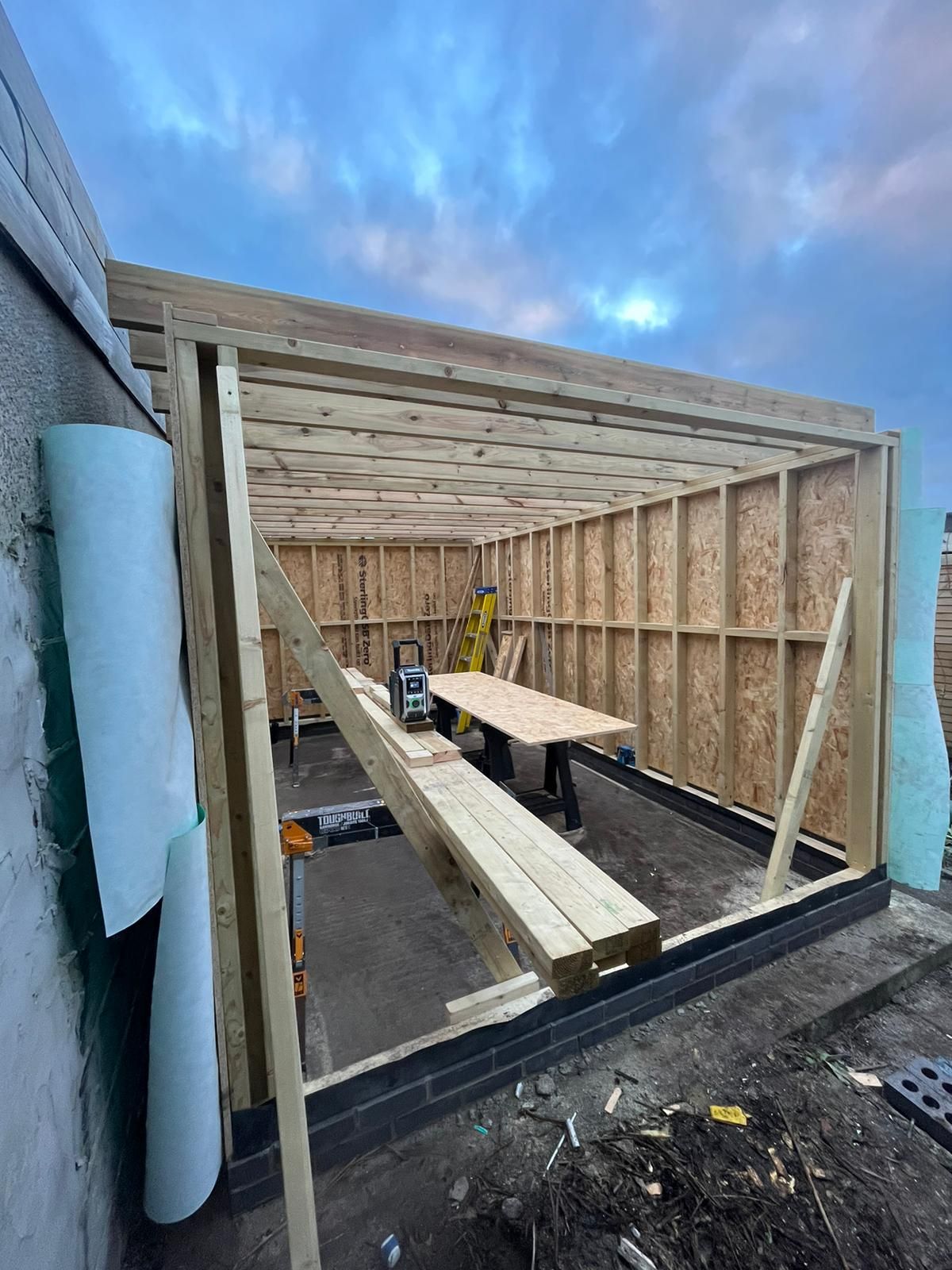 Partially built wooden frame structure on a rooftop or deck at dusk with exposed studs and beams