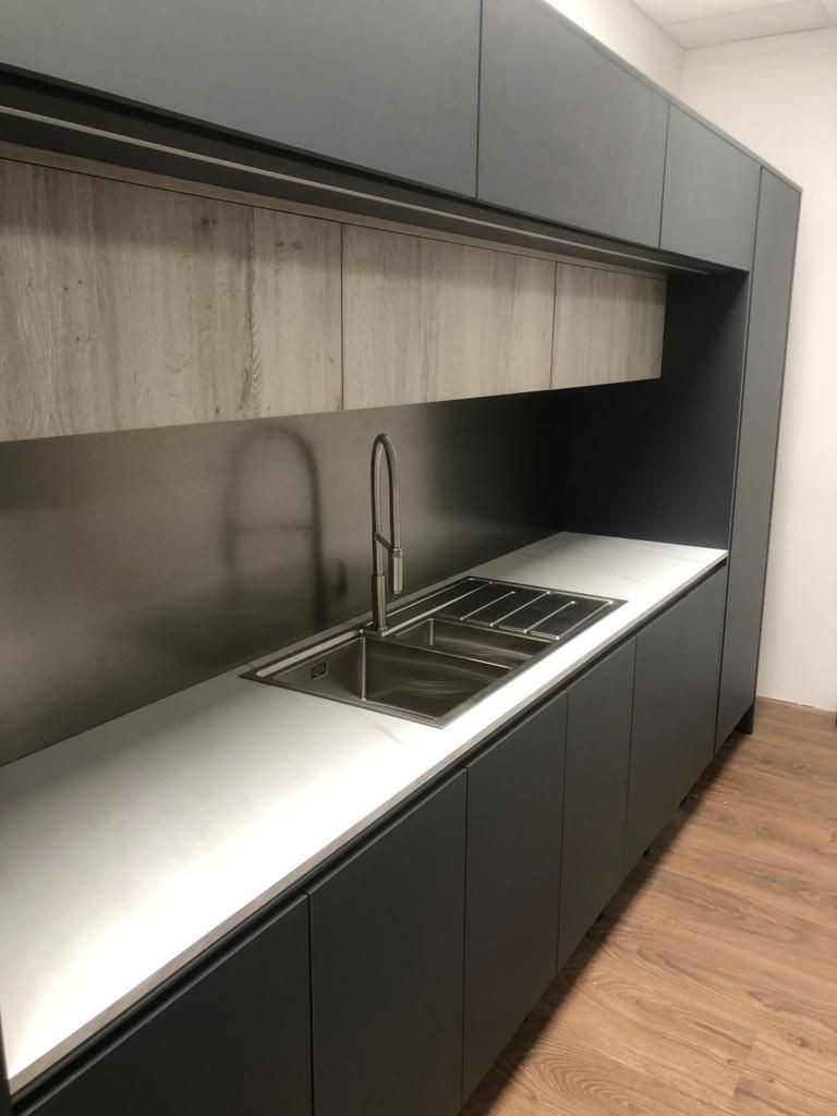 Modern kitchenette with black cabinets, white countertop, sink, stovetop, and wood flooring