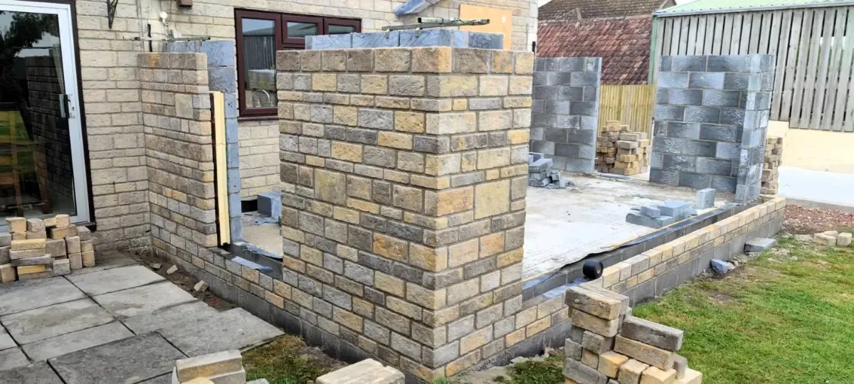 Partially built brick wall foundations at a construction site with paving stones and grass nearby