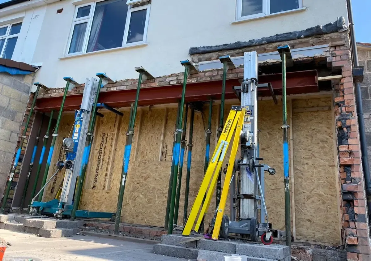 Building facade under renovation with scaffolding, boarded-up lower windows, and yellow support poles