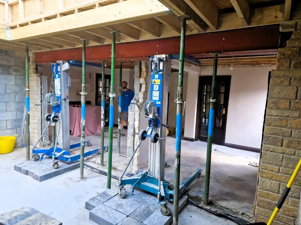 Under-construction basement with metal support posts and scaffolding in a room with exposed beams and stone walls