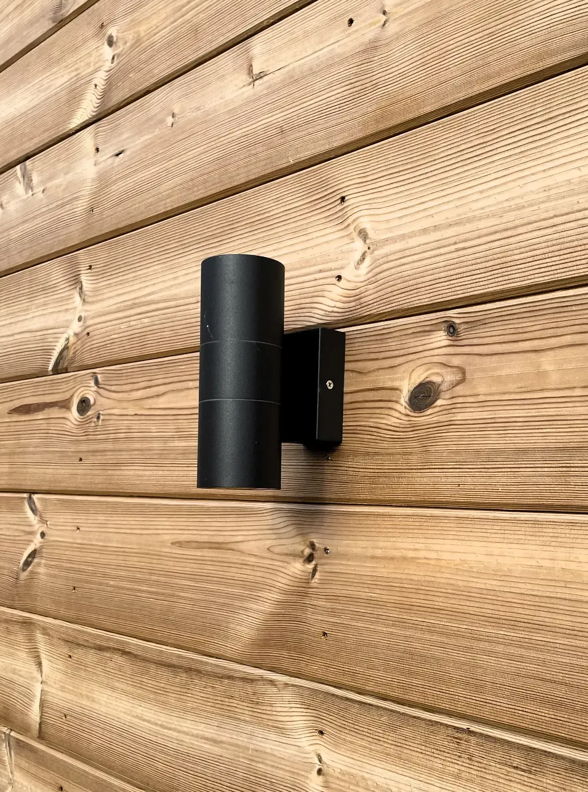 Black wall-mounted outdoor light on a rustic wooden wall