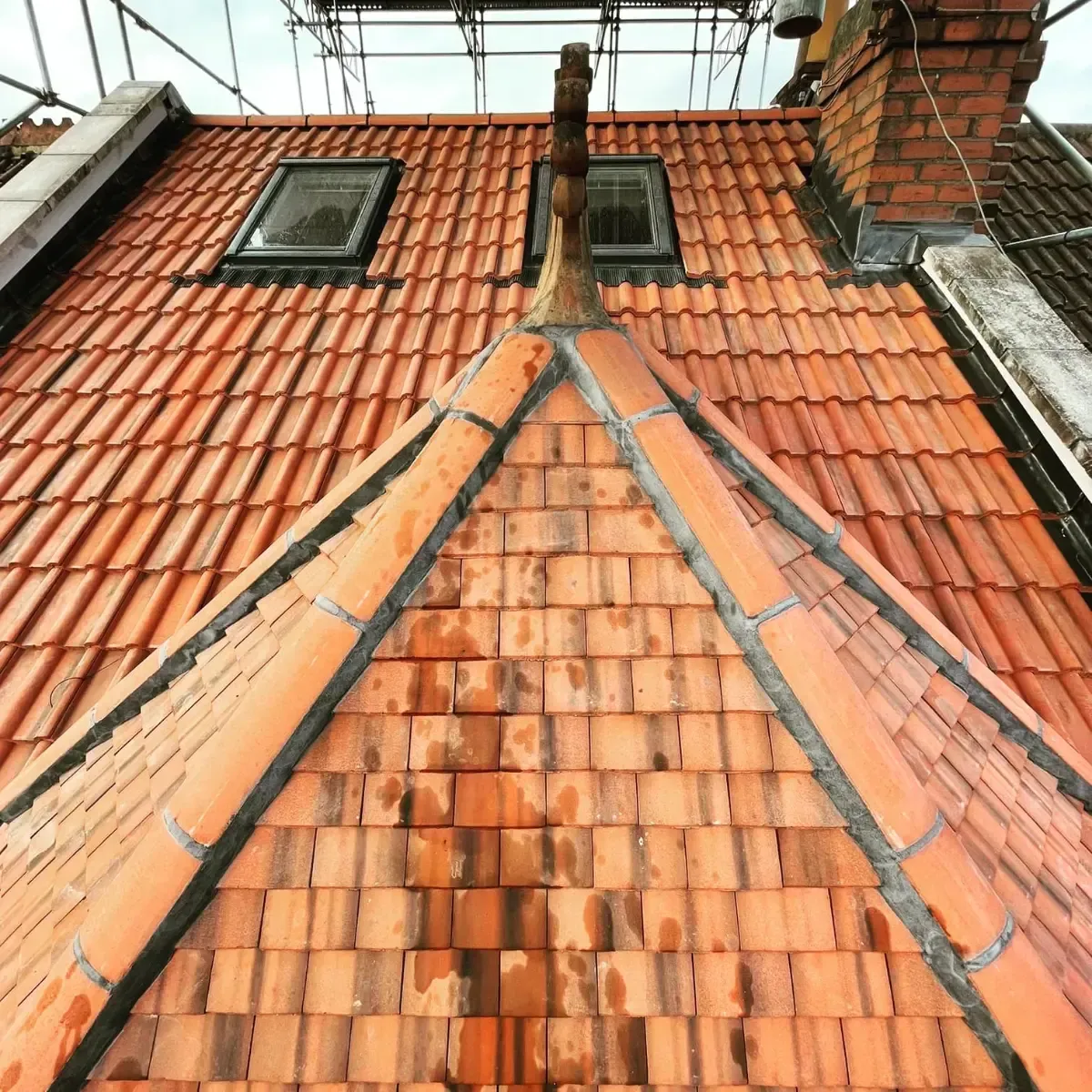 Red-tiled rooftop with dormer windows and a chimney under construction.