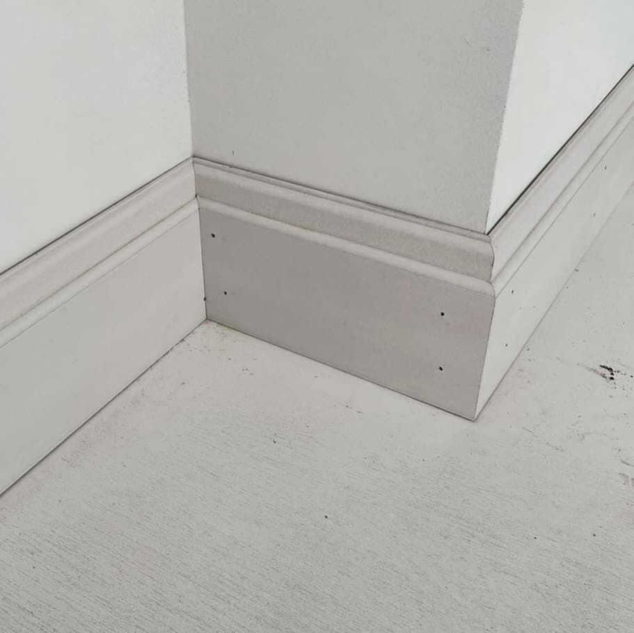 White baseboard molding at an interior wall corner on a light gray floor.
