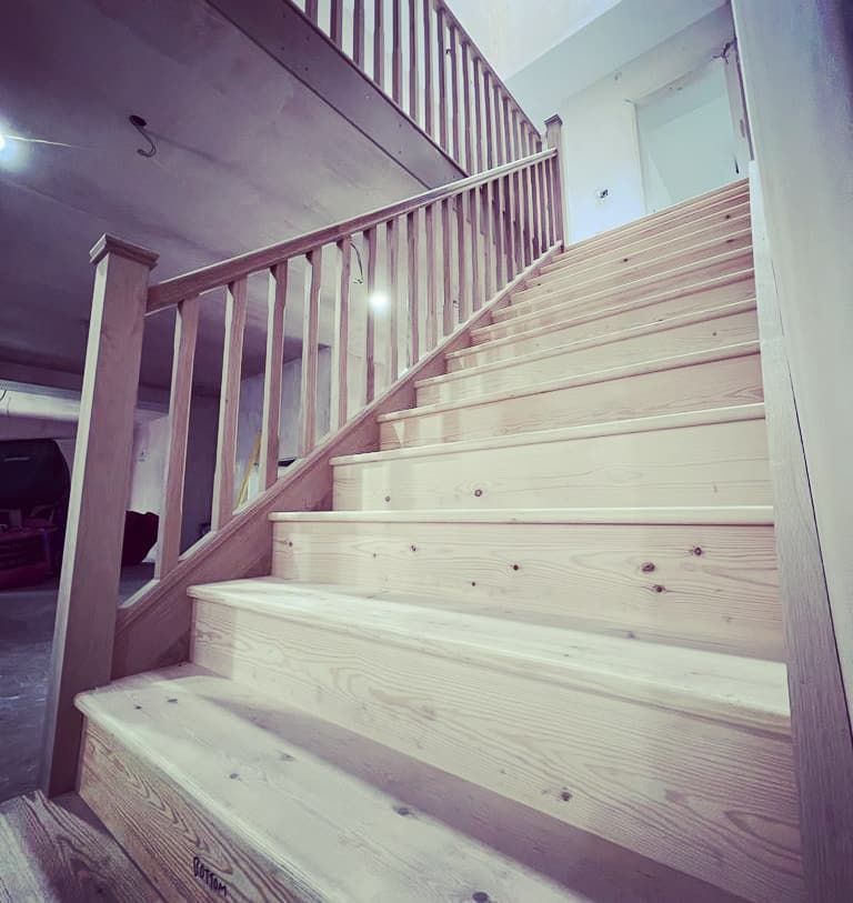 Wooden staircase with white railings leading upward in a bright indoor hallway