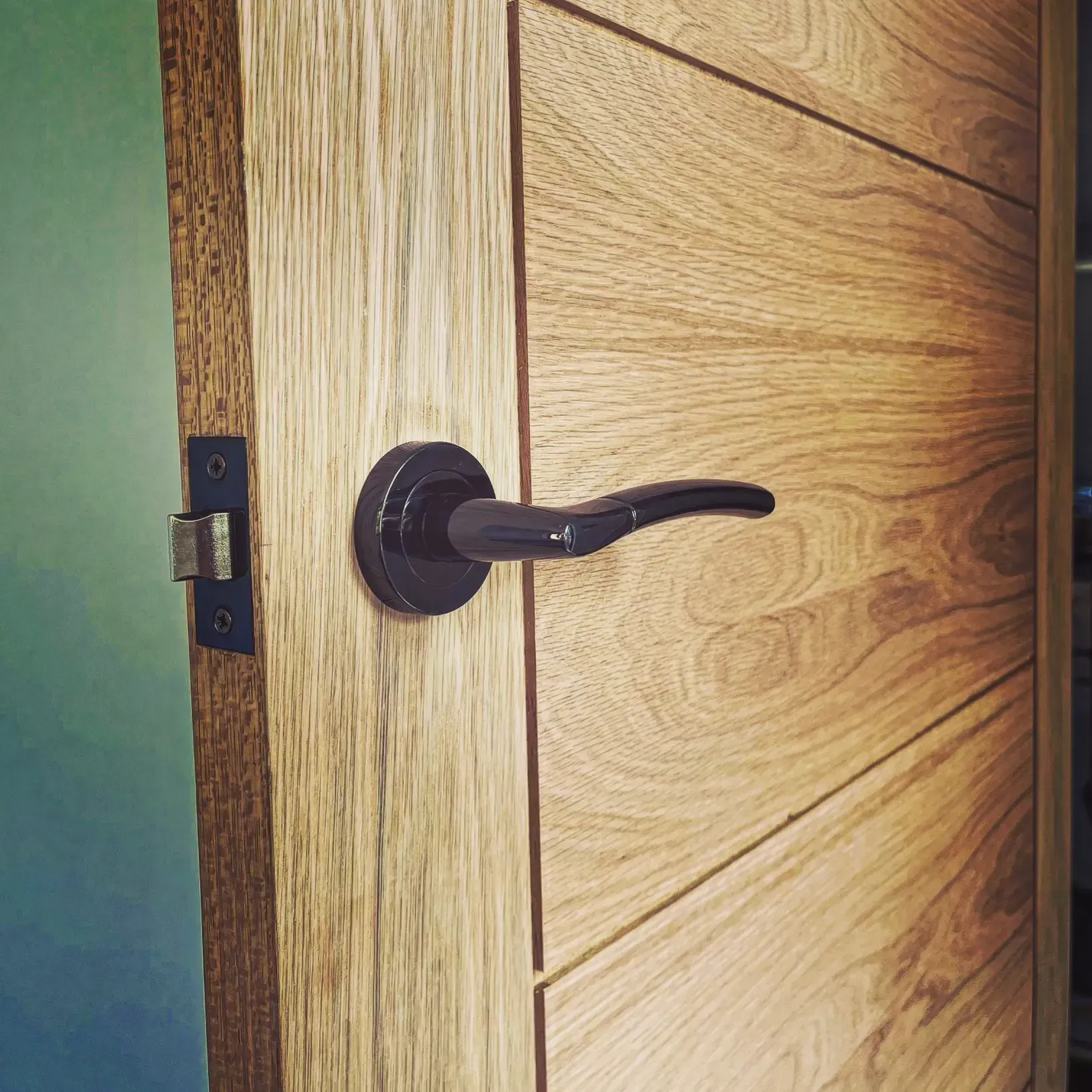 Close-up of a dark metal door handle on a light wood interior door partially open