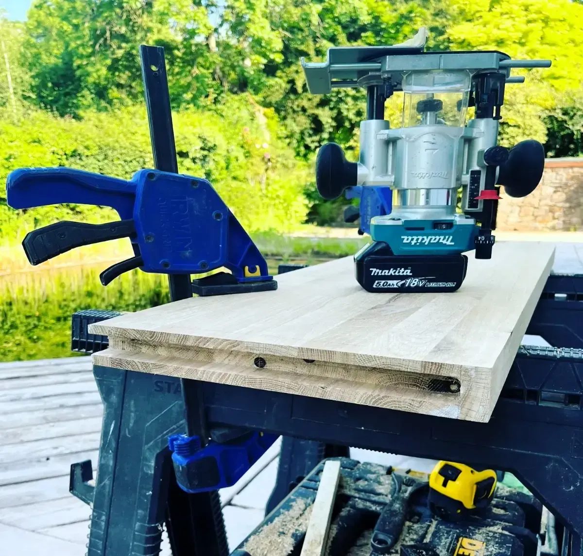 A router cutting a wooden board clamped on a workbench outdoors.