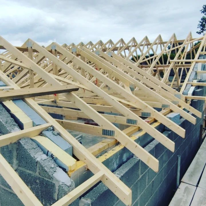 Roof trusses under construction on a cinder block building, with pale wood framing and blue sheeting.