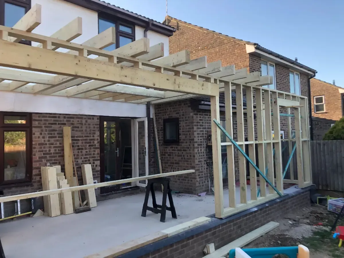 Backyard patio with a partially built wooden pergola attached to a brick house