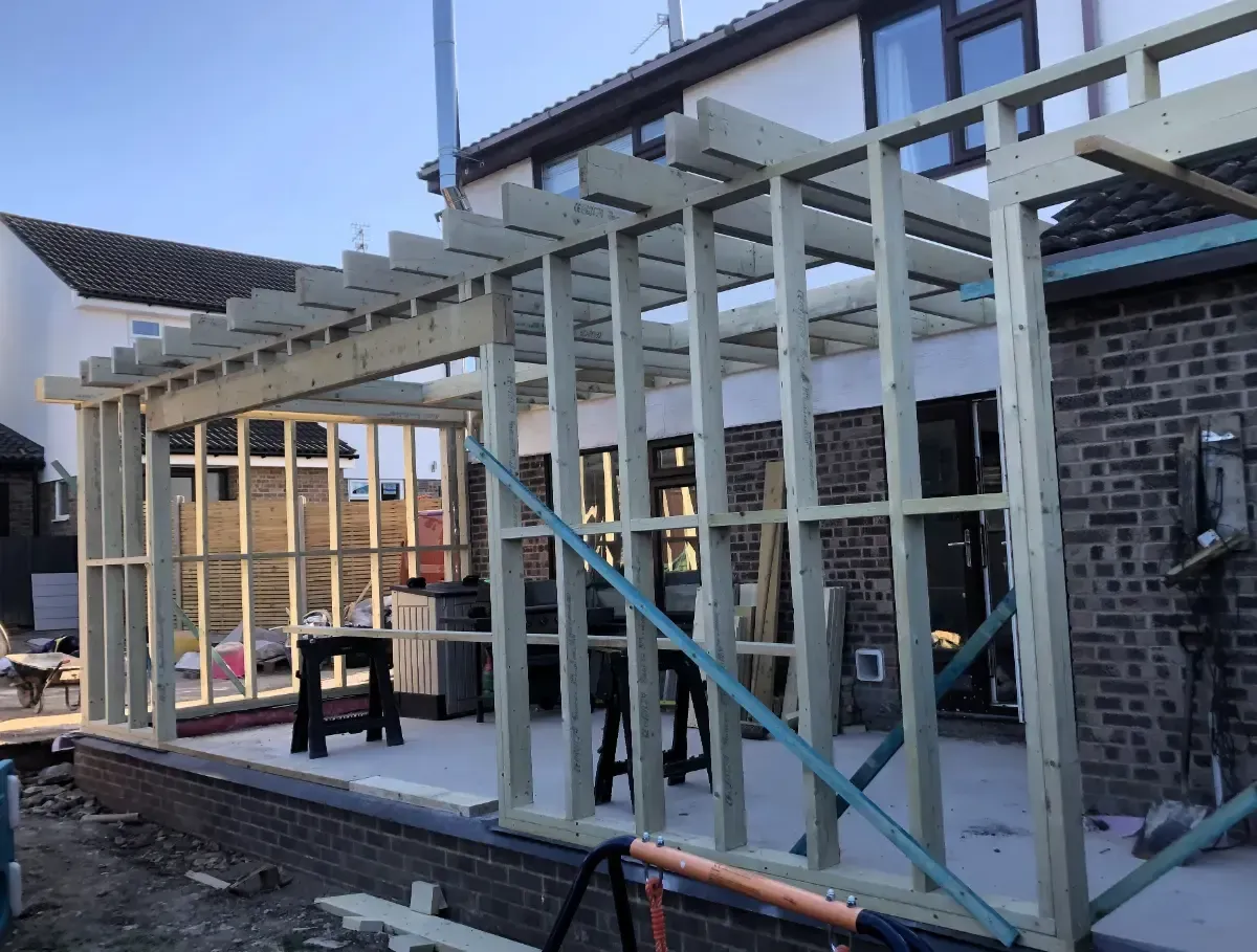 Partially built house extension with wooden frame, brick walls, and a ladder in the foreground