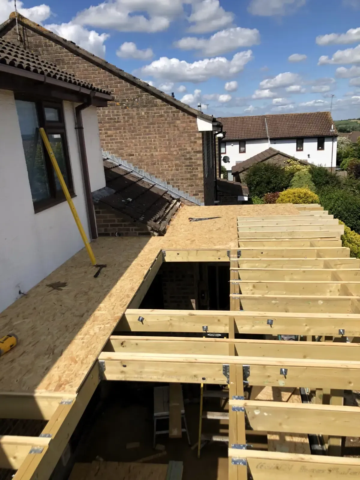 Partially built wooden roof deck beside a brick house under a cloudy sky