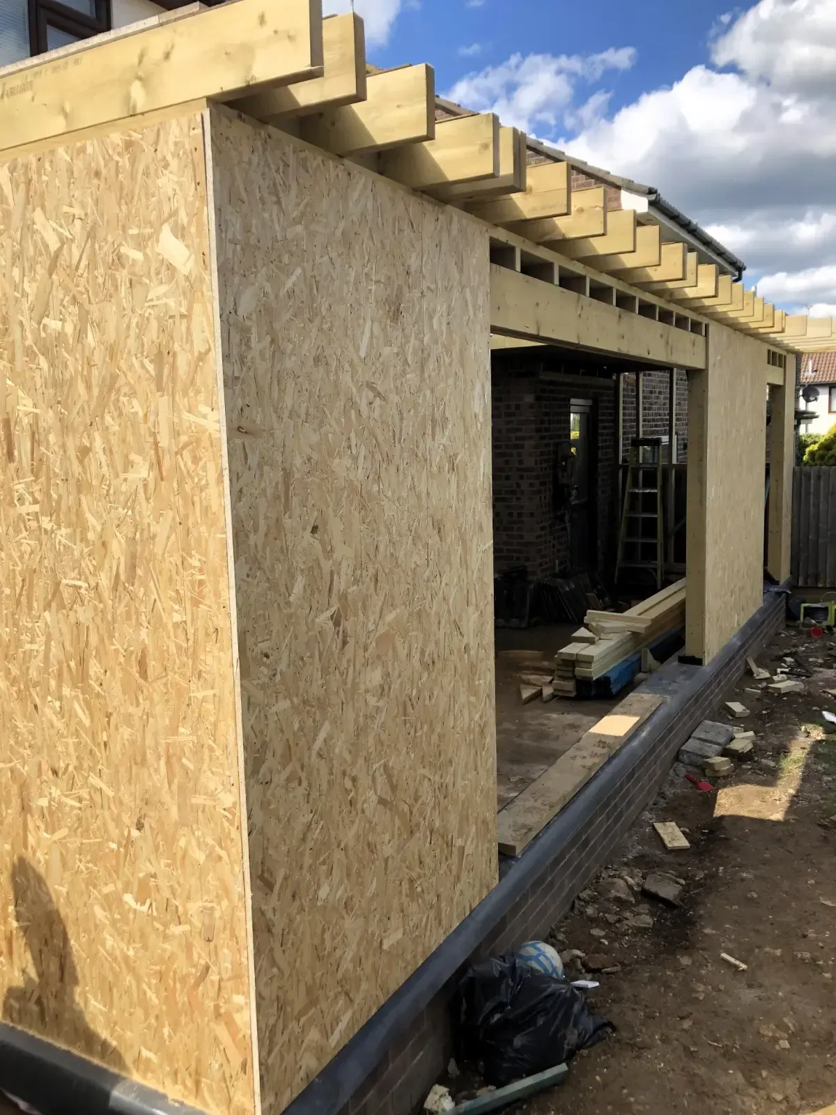 Construction site with OSB-clad building under construction and exposed roof framing.