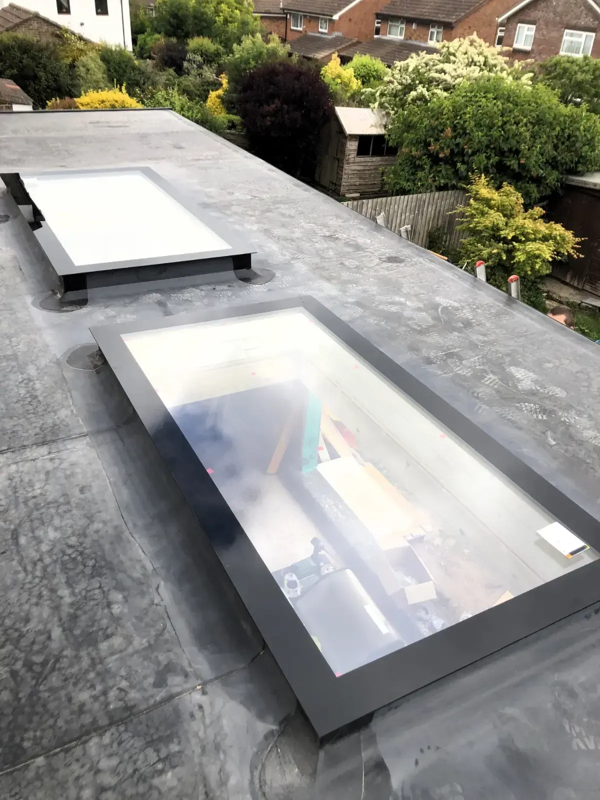 Rooftop skylights on a flat gray roof with trees and a house in the background