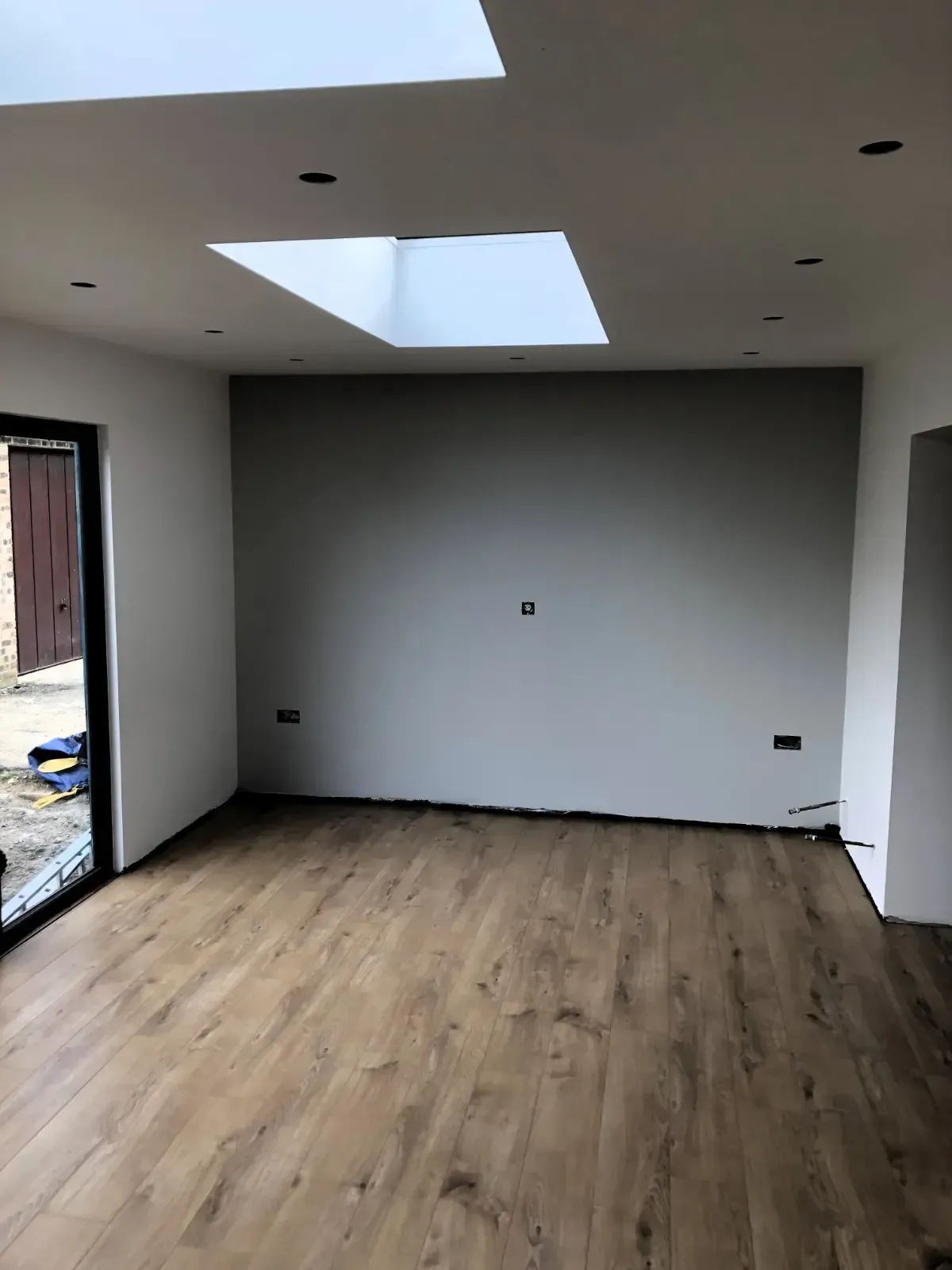 Empty modern room with wood floors, white walls, and skylights, viewed from an open doorway.