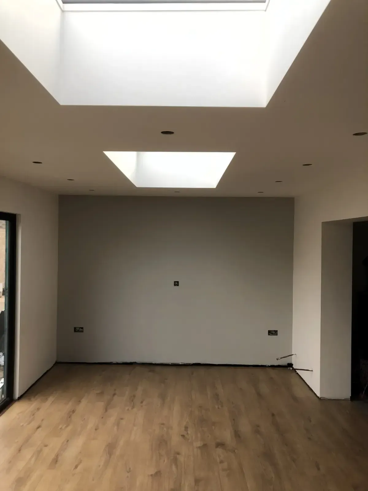 Empty modern room with wood floor, gray walls, and large skylights.