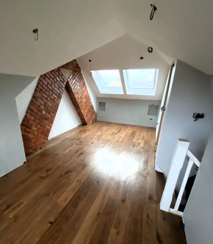Empty attic room with slanted white walls, exposed brick, skylights, and wooden floor