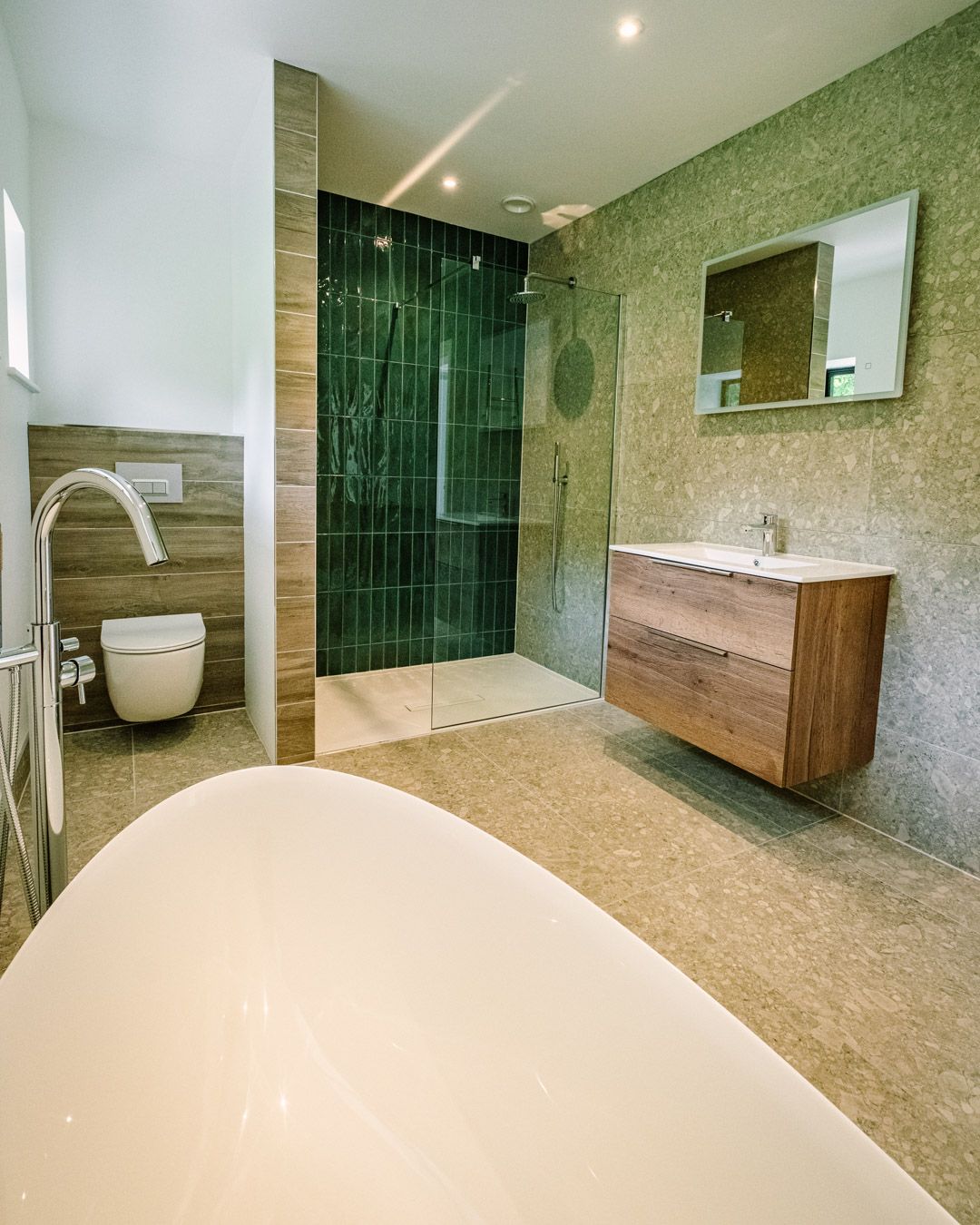 Modern bathroom with freestanding tub, glass shower, wood vanity, and green mosaic walls