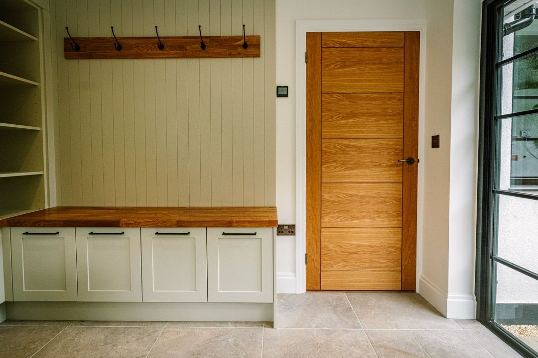 Empty entryway with a wooden door, coat hooks, bench, and tiled floor