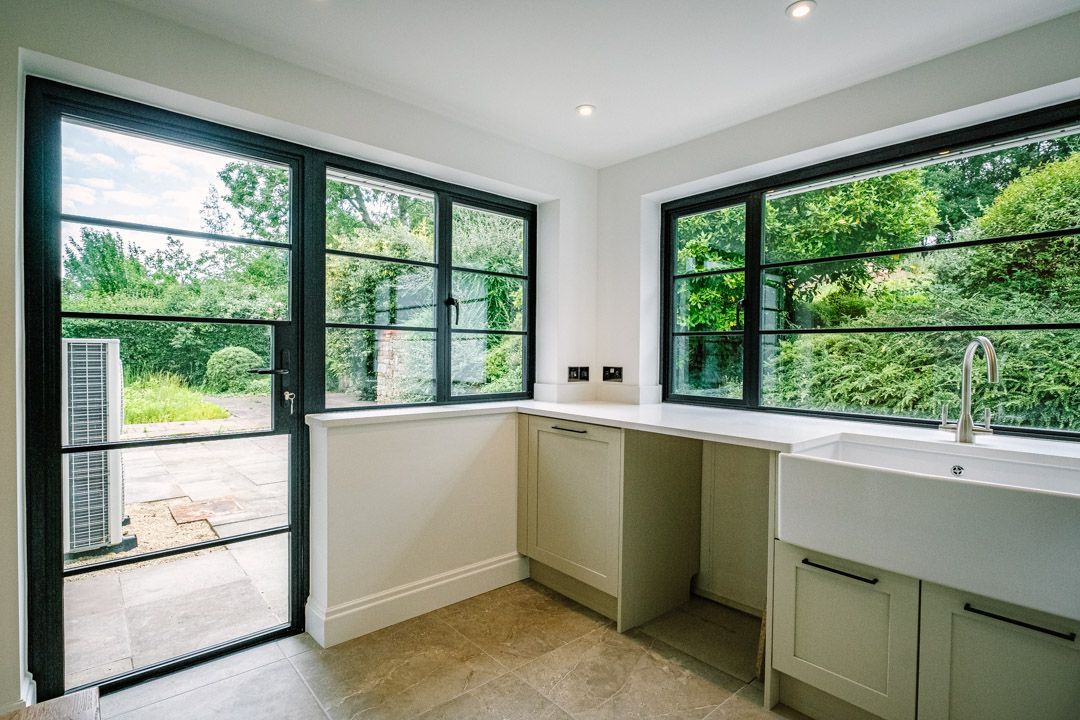Bright empty room with large black-framed windows and built-in cabinets, showing a garden view