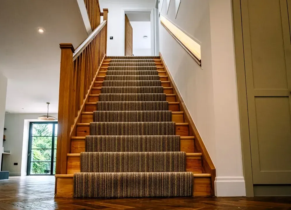 Wooden staircase with carpet runner leading to a bright hallway in a modern home